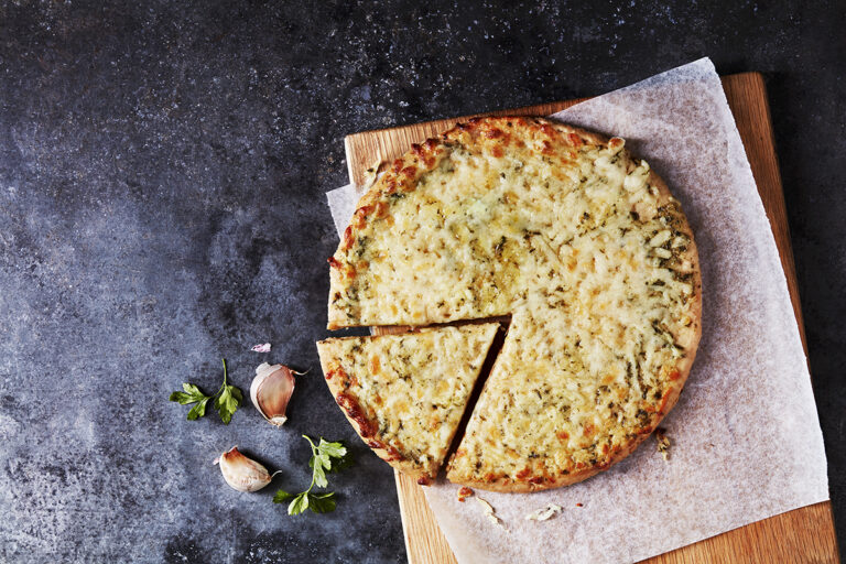 A cheese pizza with a cauliflower crust, topped with herbs and served on a wooden board.