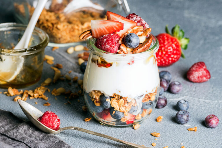 A yogurt parfait in a glass jar, layered with granola, berries, and nuts, garnished with fresh fruit.