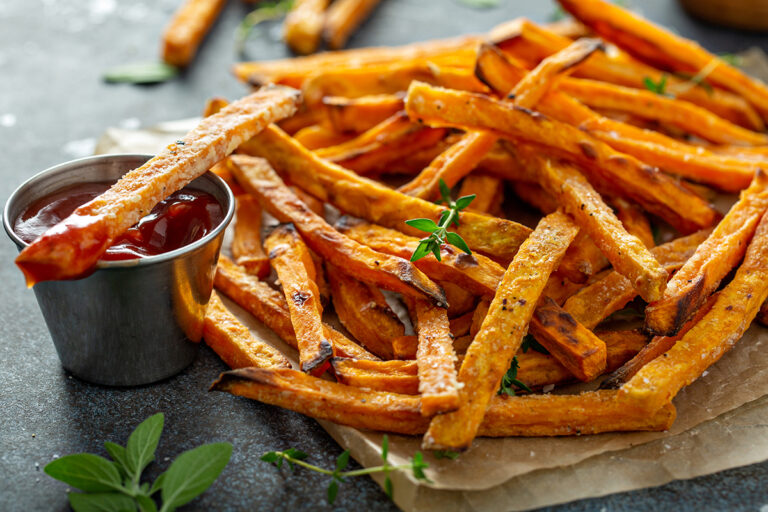 A serving of crispy sweet potato fries, seasoned and accompanied by a dip, garnished with fresh herbs.