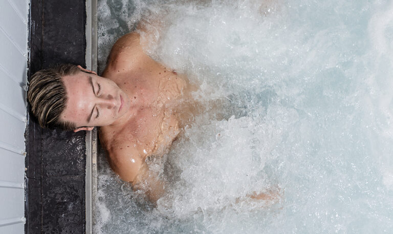 A man relaxing in an ice bath, with water swirling around him, highlighting the practice of cold water immersion.