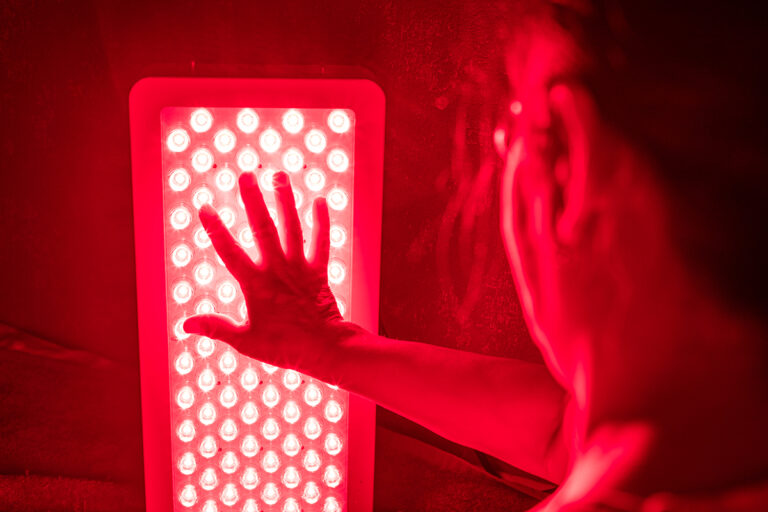 A person holding their hand up to a panel emitting red light, showcasing the benefits of red light therapy.