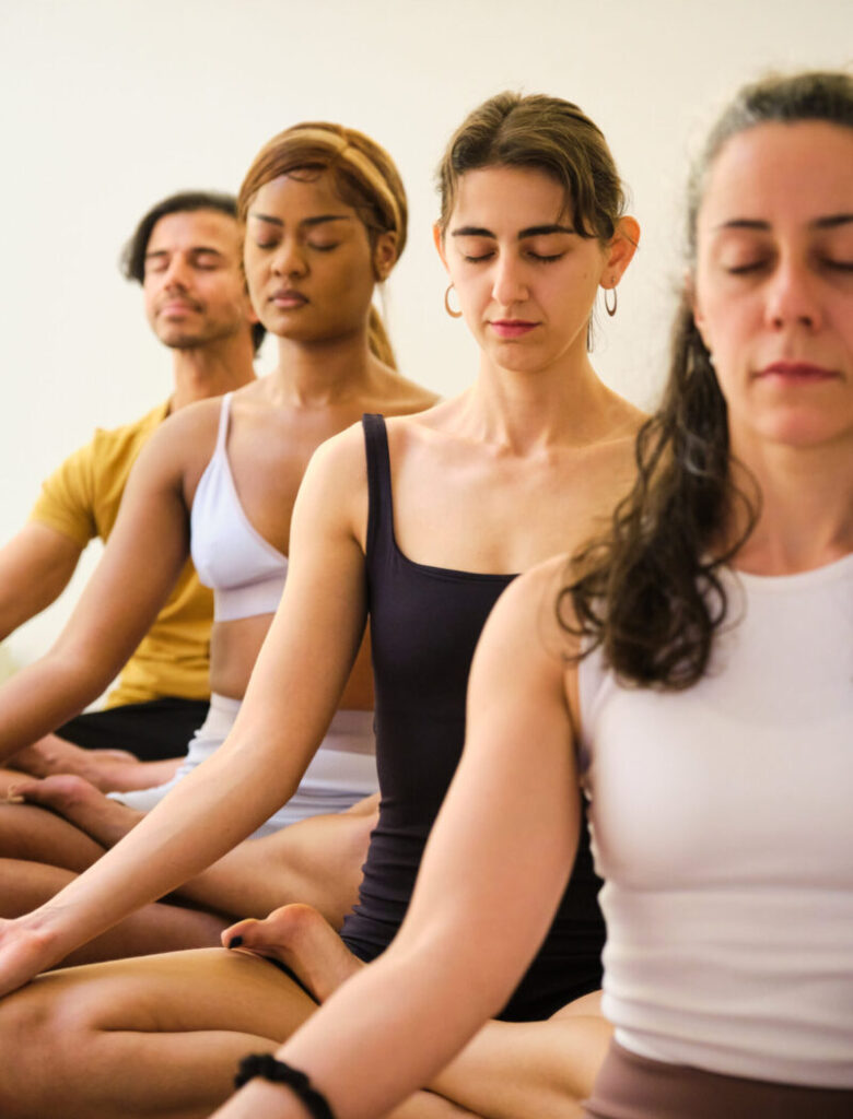 Group of people meditating in seated lotus pose, eyes closed in sacred stillness at The Yoga Spa