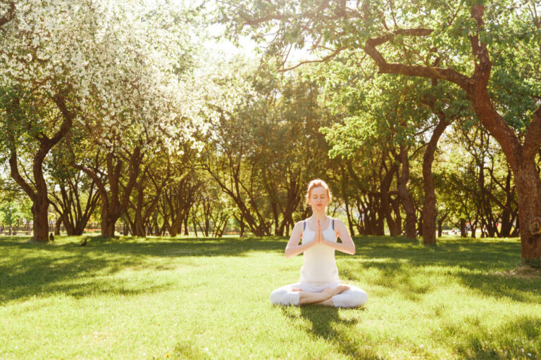 Woman meditating outdoors in a sunlit park, embodying awaken and align energy